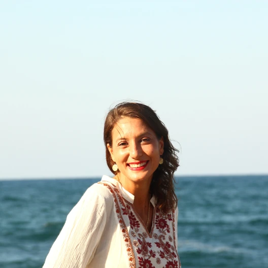Anna in a white, flowery top with the ocean in the background