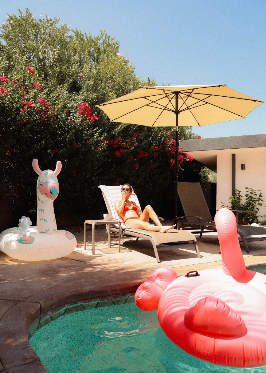 A girl sitting next to a pool with a flamingo floatie. 