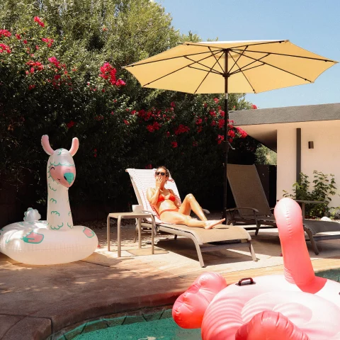 A girl sitting next to a pool with a flamingo floatie. 