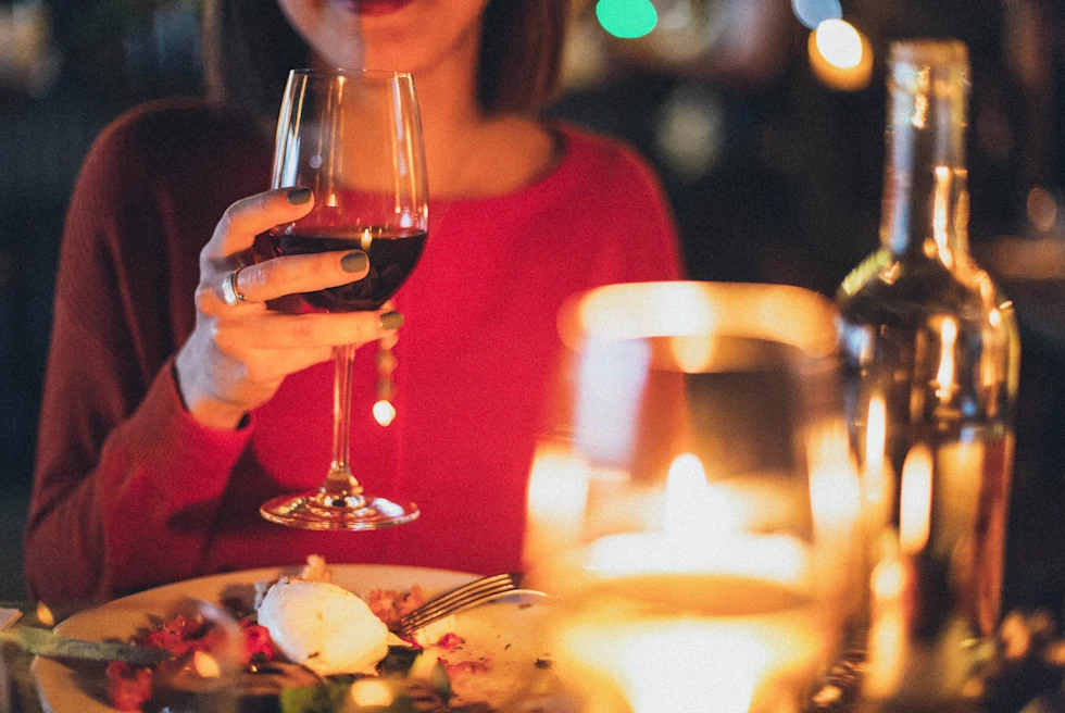 A girl drinking wine and a plate of food in front of her on the dinning table