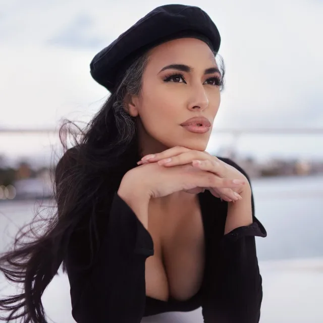 Travel Advisor Alexia Lim with a black hat and shirt in front of a lake.