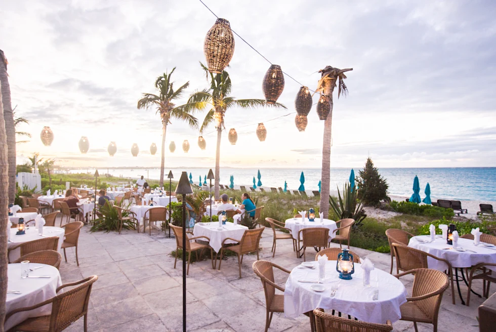 Tables and chairs on outdoor patio with palm trees and ocean with cloudy skies