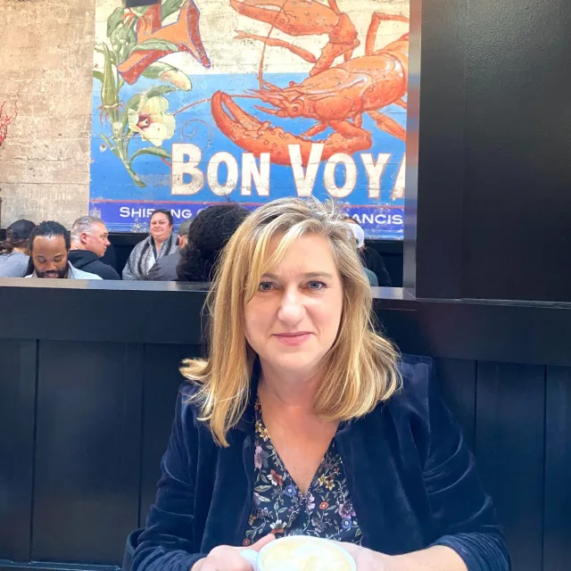 Travel Advisor Lara Kudryk Traska sitting in a restaurant in navy blazer. 