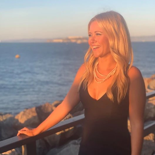 Travel Advisor Jessica Leary in a black dress and pearl necklace, standing in front of the water.