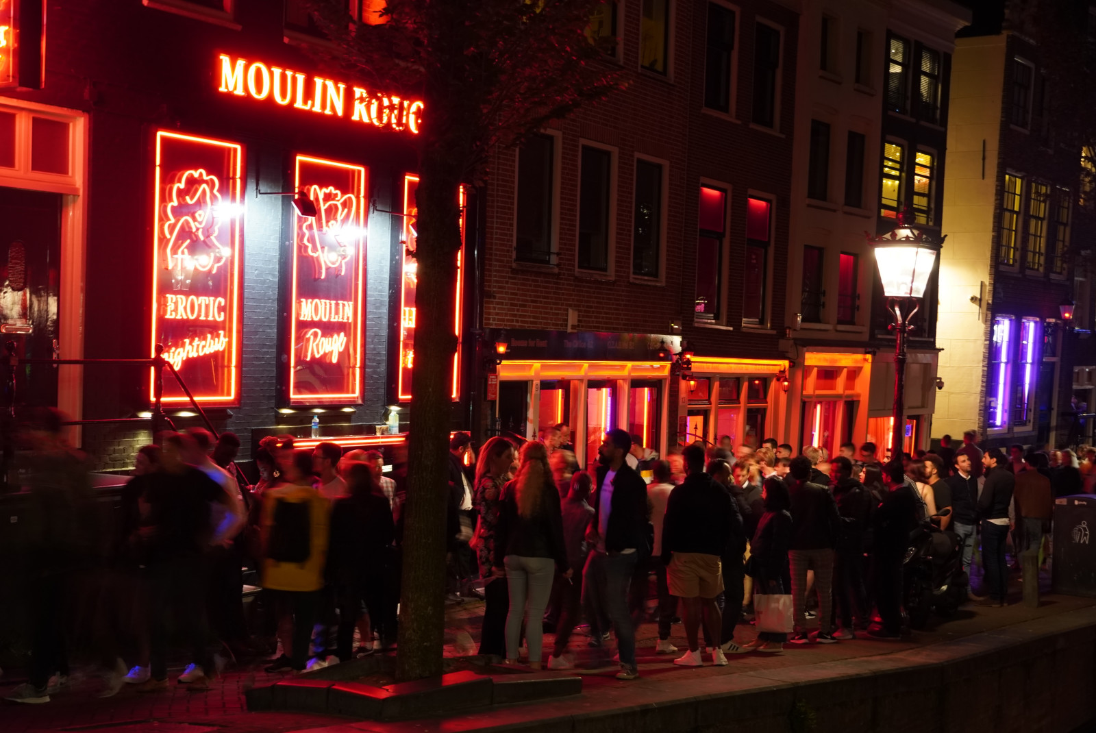 People standing on the streets next to building with red lights during nighttime