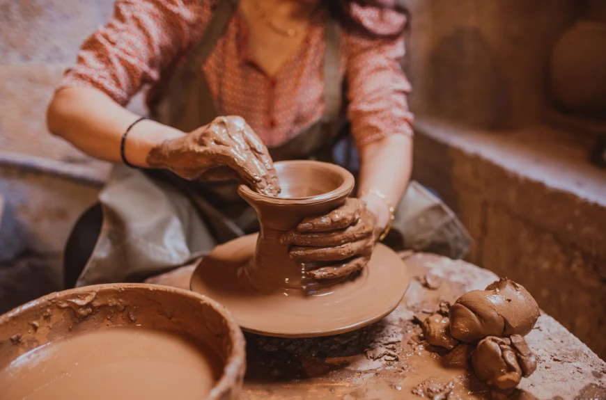 a woman molds wet clay on a spinning wheel