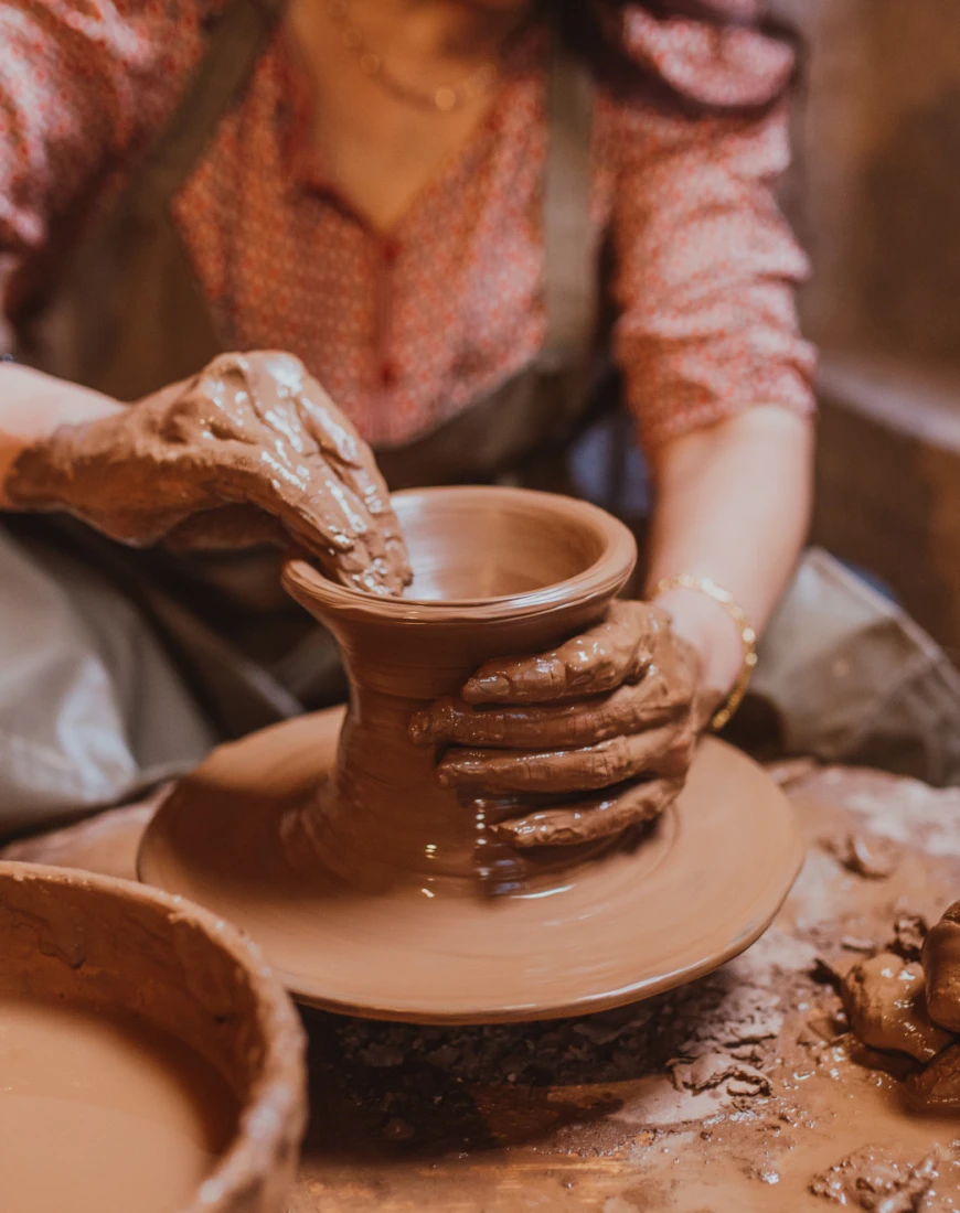 a woman molds wet clay on a spinning wheel