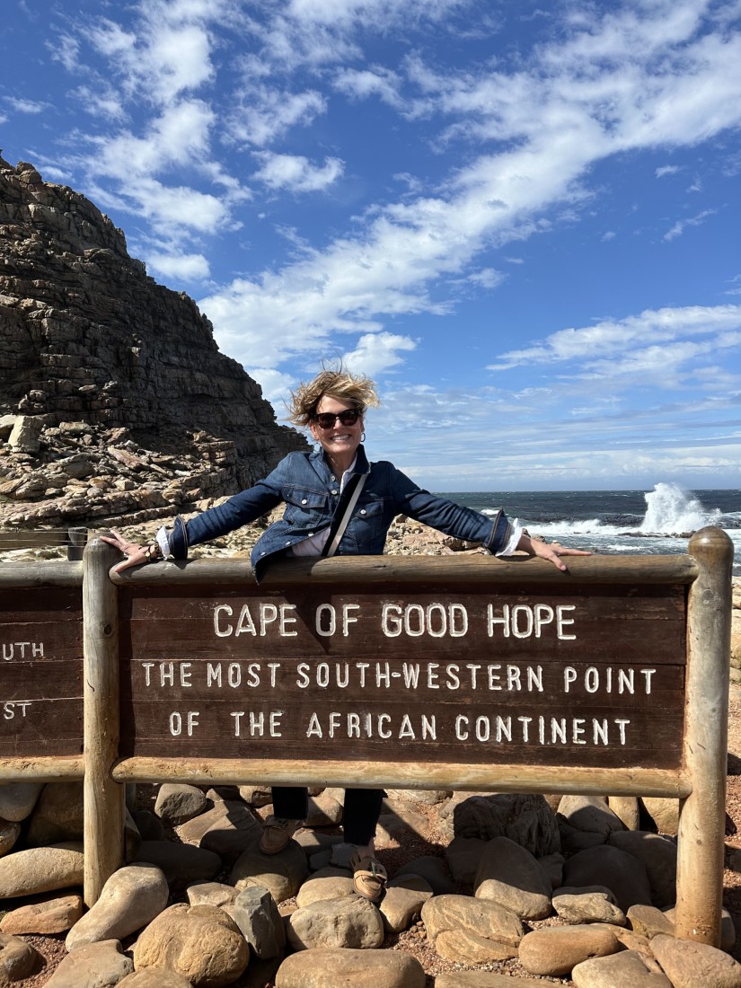 Travel advisor posing and smiling behind the sign at the Cape of Good Hope on a windy, yet sunny day.