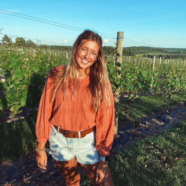 Travel Advisor Morgan Blaylock wears an orange top and jean shorts in a wine vineyard