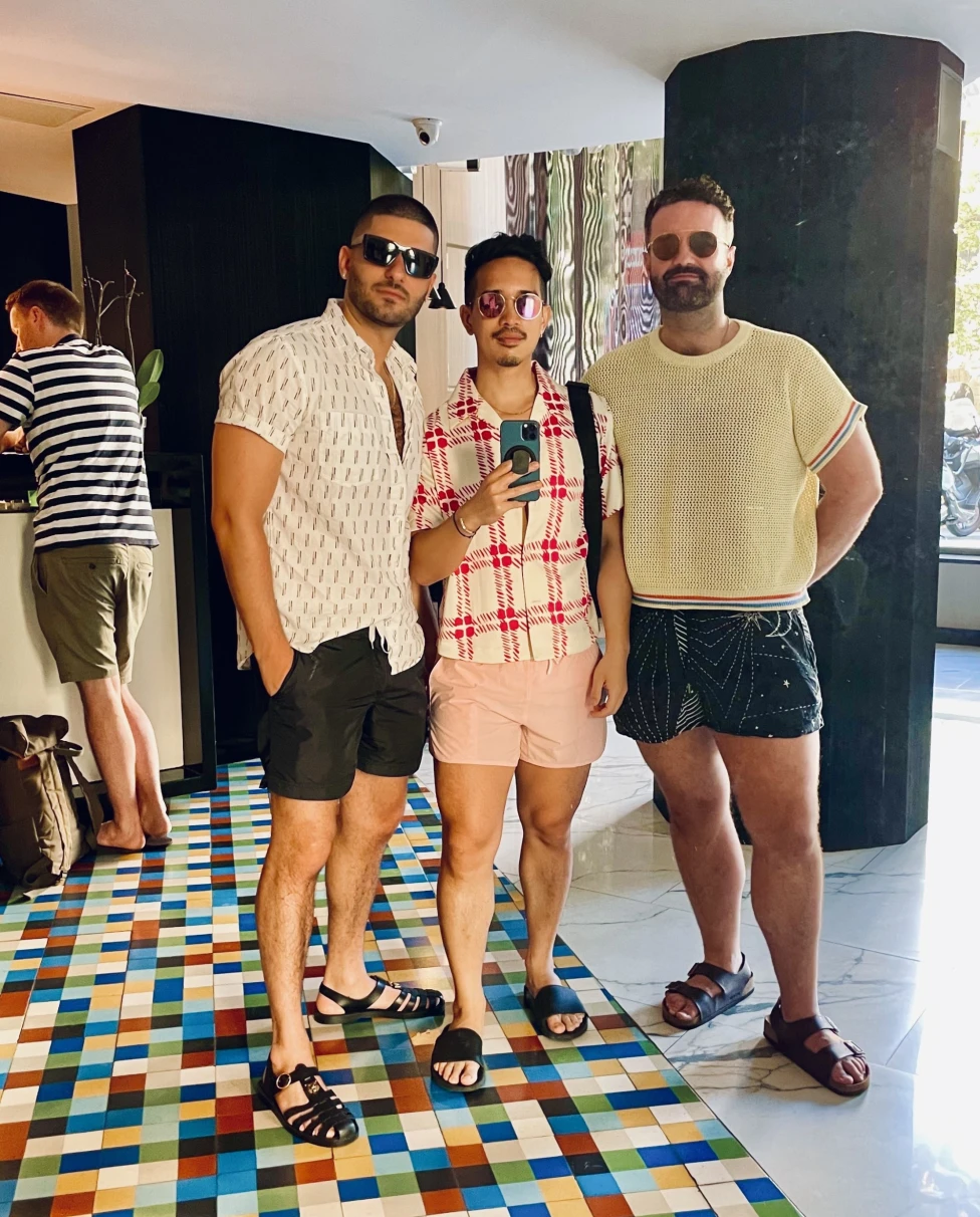 Three men dressed in tshirts and shorts, wearing sunglasses, standing on a colorful floor.