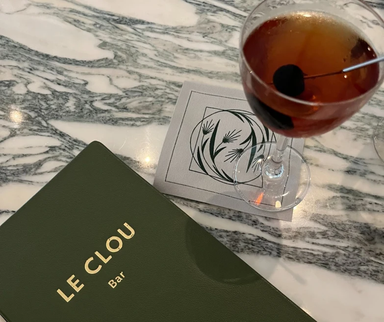 a menu book reads, "LE CLOU" with a martini sitting beside it on a marble bar