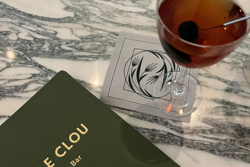 a menu book reads, "LE CLOU" with a martini sitting beside it on a marble bar