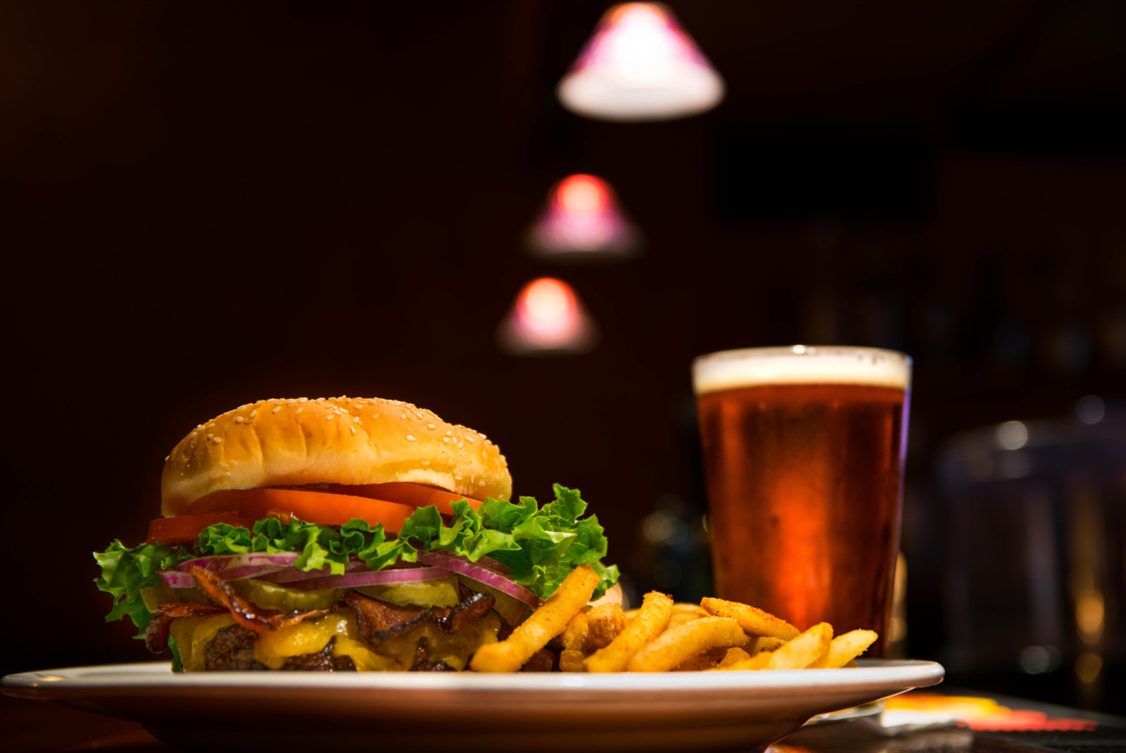 Burger with fries on a white plate with a glass of beer