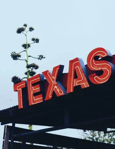 A red neon sign that reads "Texas" on the exterior of a building outside. 