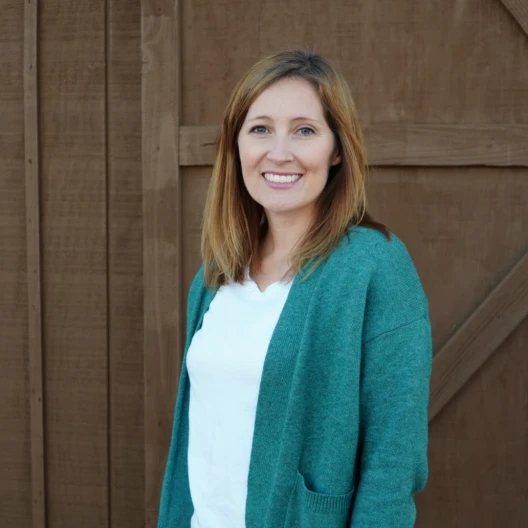 Travel Advisor Andrea Taylor in front of a brown wooden door and wearing a white shirt and green cardigan.