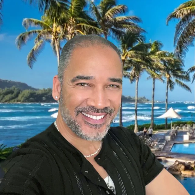 Travel Advisor Marc Bailey in a black shirt with palm trees and the beach in the back.
