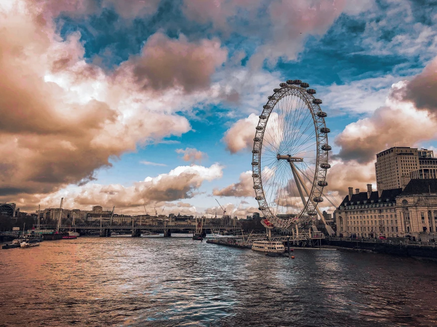 The London Eye in London, United Kingdom, England with pink clouds and the river Thames