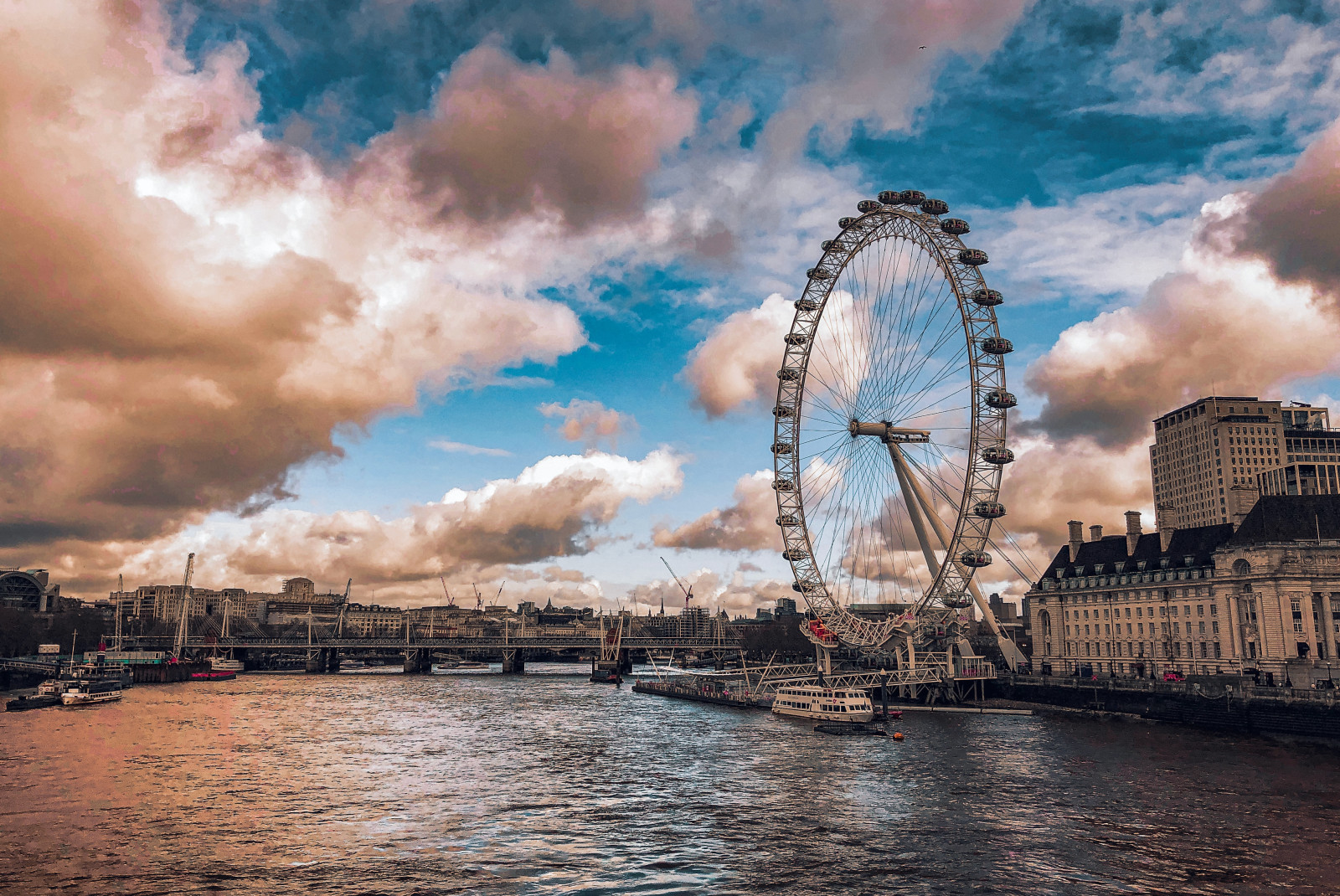 The London Eye in London, United Kingdom, England with pink clouds and the river Thames