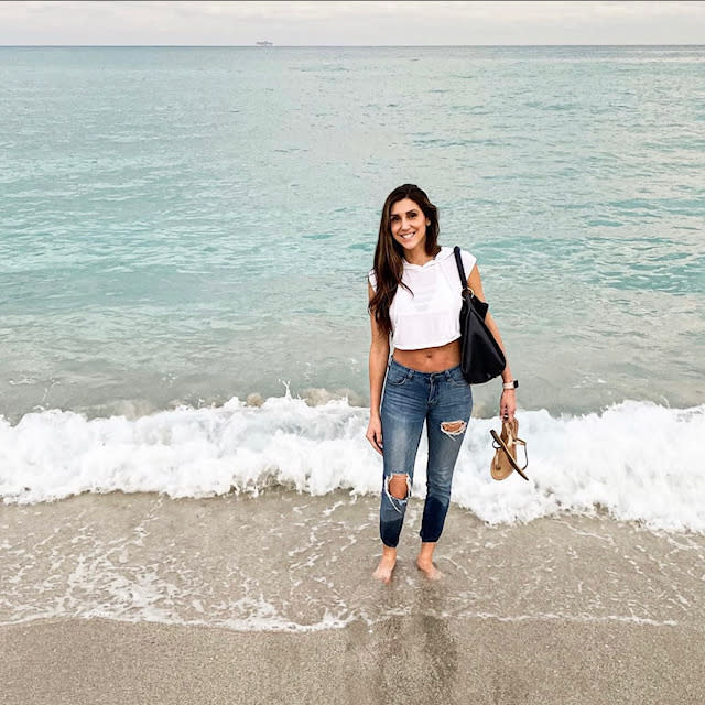 Fora travel agent Loren Schlichting wearing jeans and white shirt standing on beach