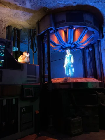 hologram of a woman being generated by a futuristic machine talking to a robot