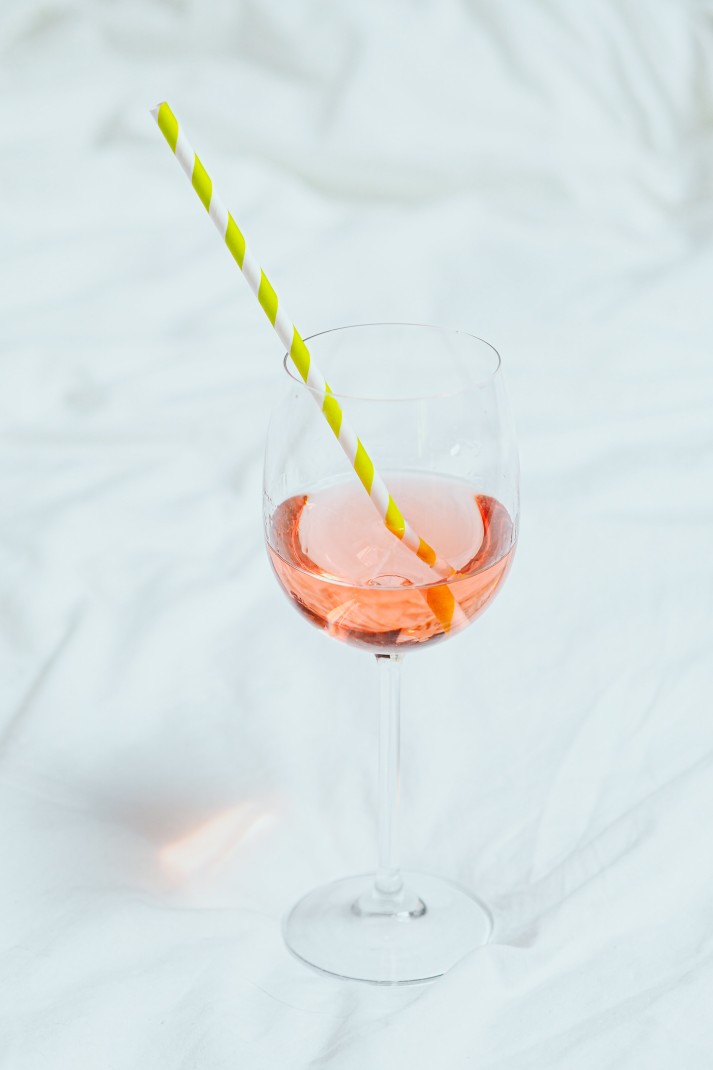Orange cocktail in wine glass with yellow and white striped straw