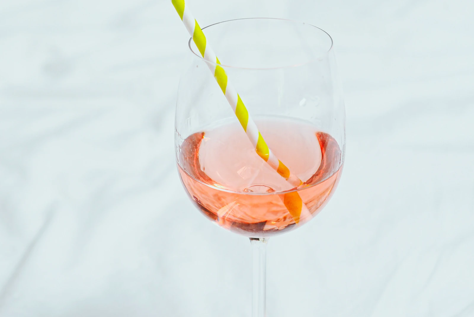 Orange cocktail in wine glass with yellow and white striped straw