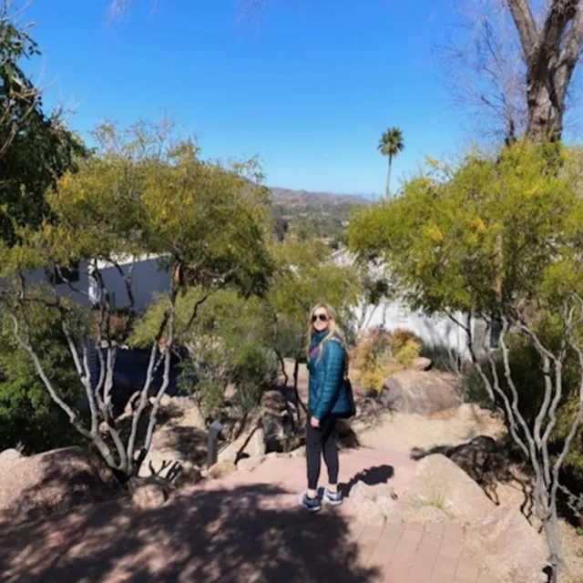 travel advisor Kara Cochran wears a turquoise jacket on hike with a blue cloudless sky