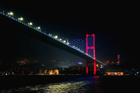 A view of the Bosphorus Bridge lit up at night before Istanbul's skyline.