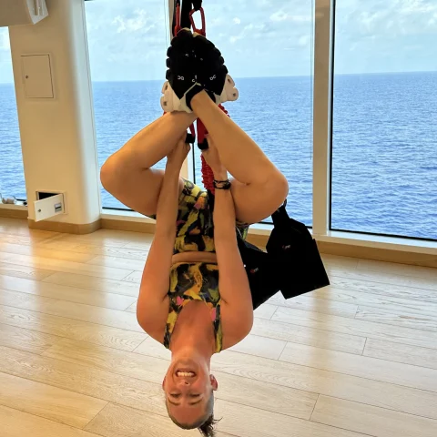 A girl hanging upside down by a rope with blue water in the background.
