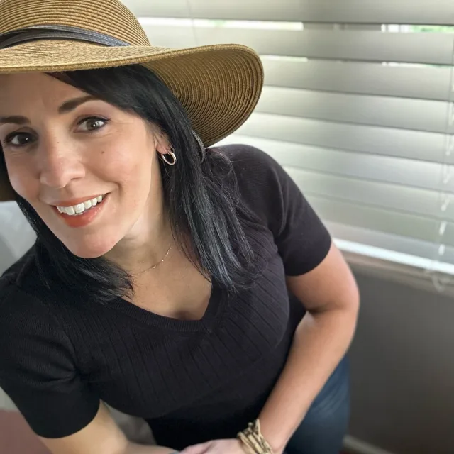 travel advisor Jennifer DiDonna in a tan hat and black shirt in front of window blinds