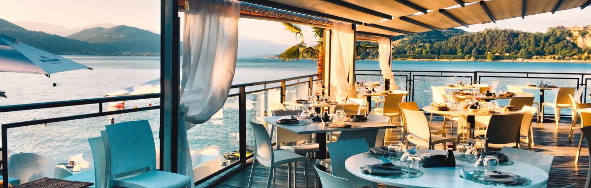 White tables and chairs on a wooden deck at a restaurant overlooking the water and mountains
