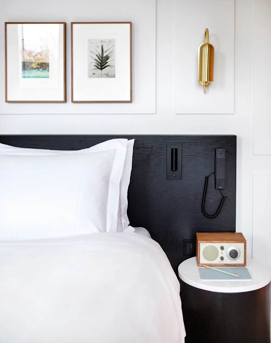 close-up of a white bed with a black headboard next to a wooden end table with an old-fashioned radio