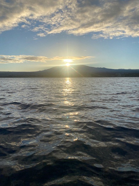 A picture of a bright sunset over a volcano in the distance. There is rippling water in the forefront. 