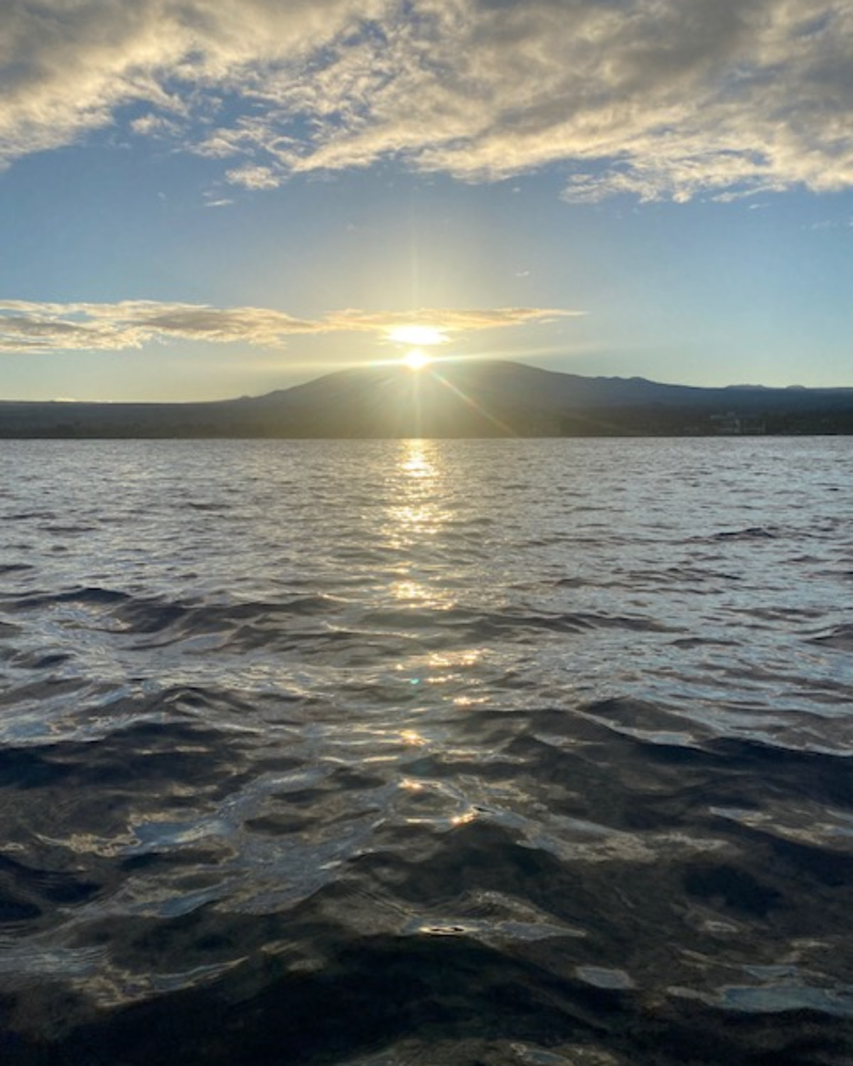 A picture of a bright sunset over a volcano in the distance. There is rippling water in the forefront. 
