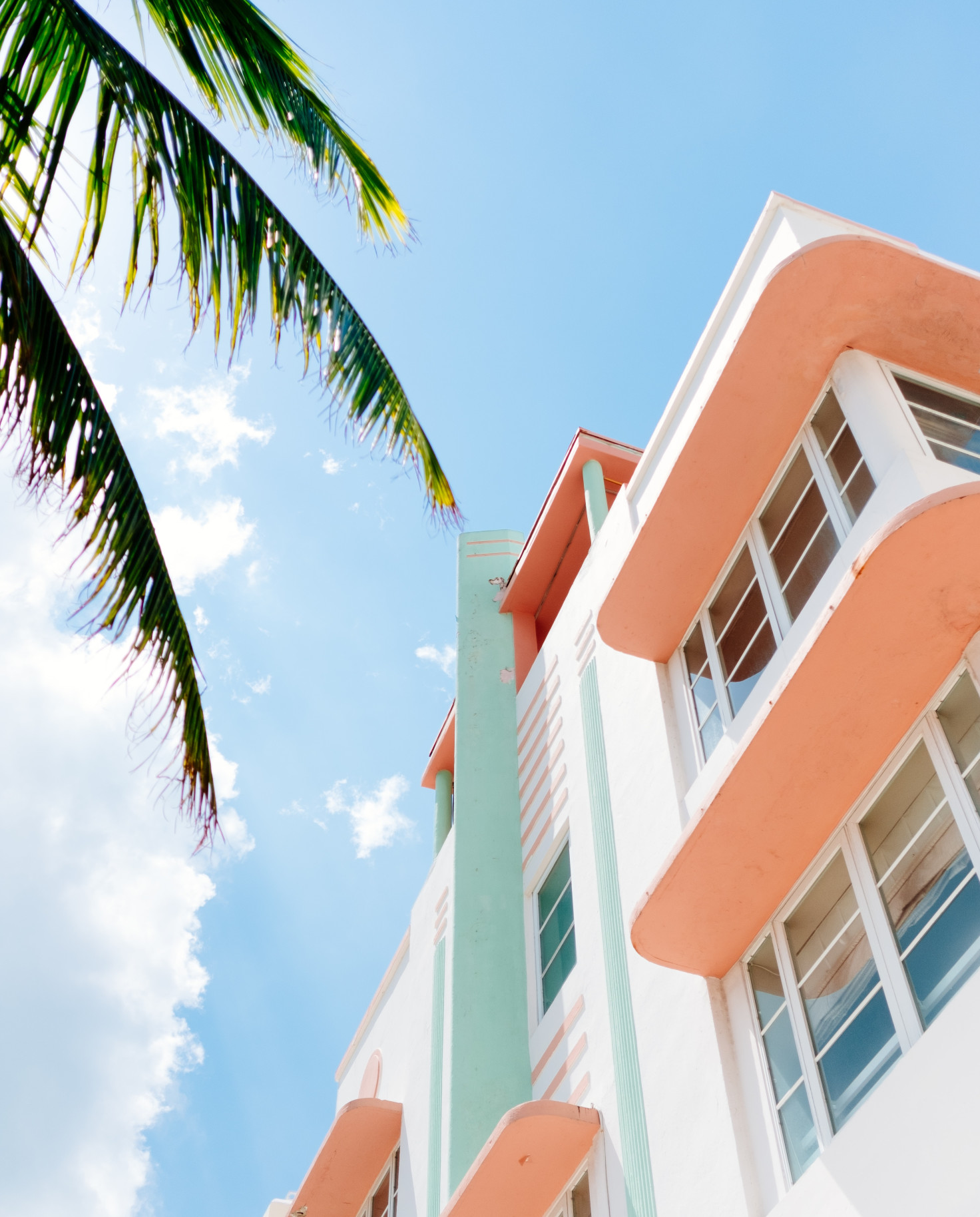 View of coral and white building next to a palm tree with a blue sky