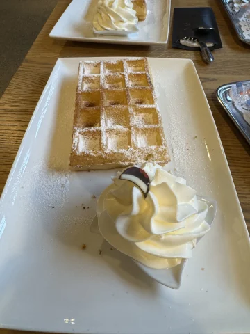 Plates of Belgian Waffles and cream, topped with powdered sugar.
