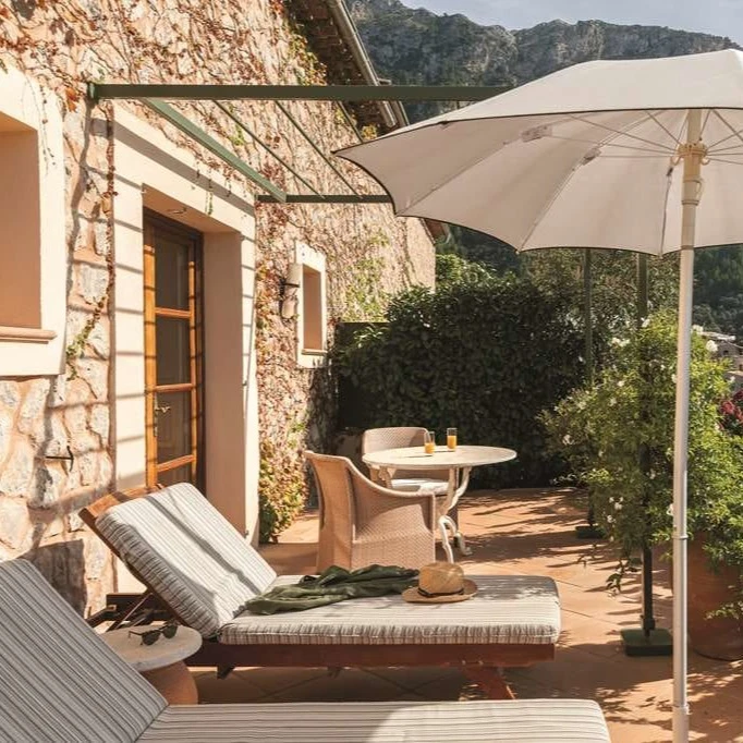 lounge chairs under a white umbrella on a sunny balcony overlooking a lush mountain