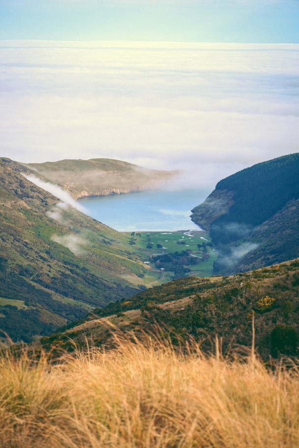View of green mountainside next to ocean with clouds and blue sky