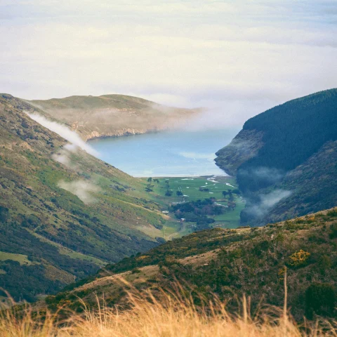 View of green mountainside next to ocean with clouds and blue sky