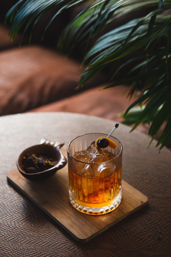 Whisky cocktail on a wooden table next to green plant