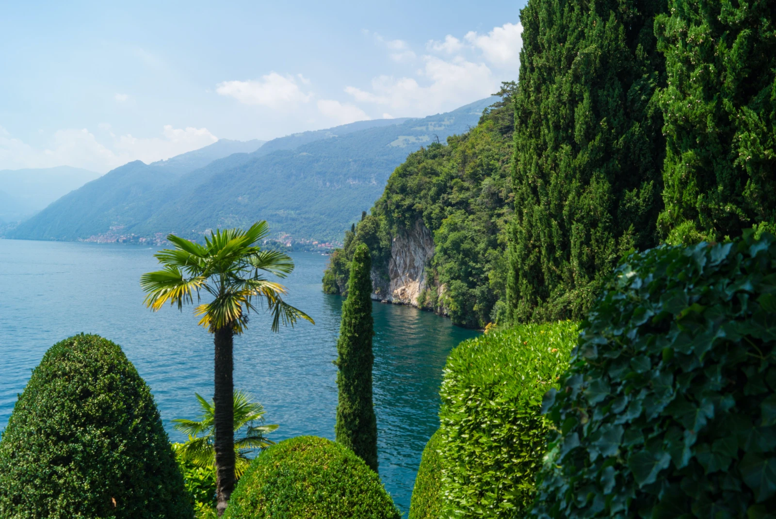 Tall green trees with blue water and cliffs at Lago di Como in Lake Como Italy.