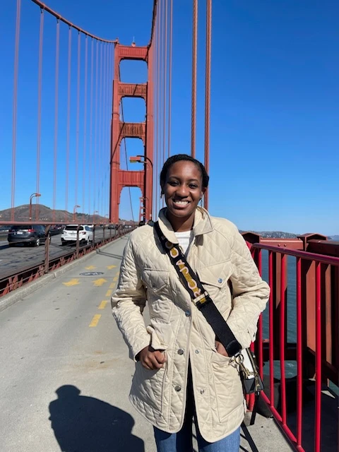 a woman in a tan jacket stands in front of a red bridge