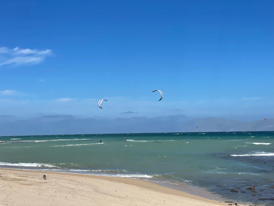 beach next to body of water with two kites in the sky