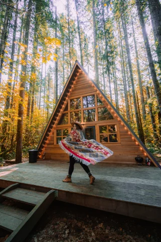 A girl is posing in front of a framed wooden cabin during the daytime.
