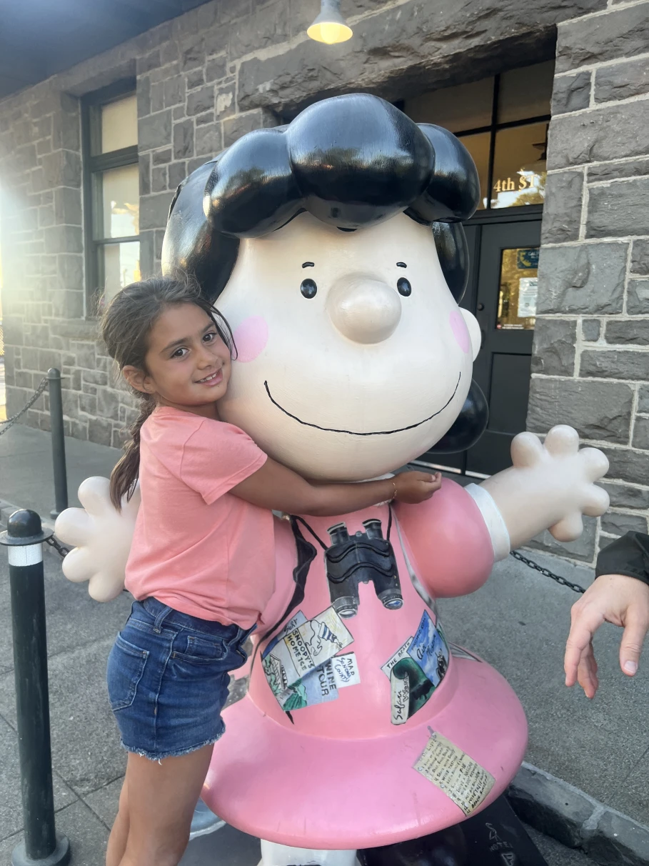 A girl in a pink t-shirt hugging a statue of Lucy from Peanuts at the Charles M. Schulz Museum.