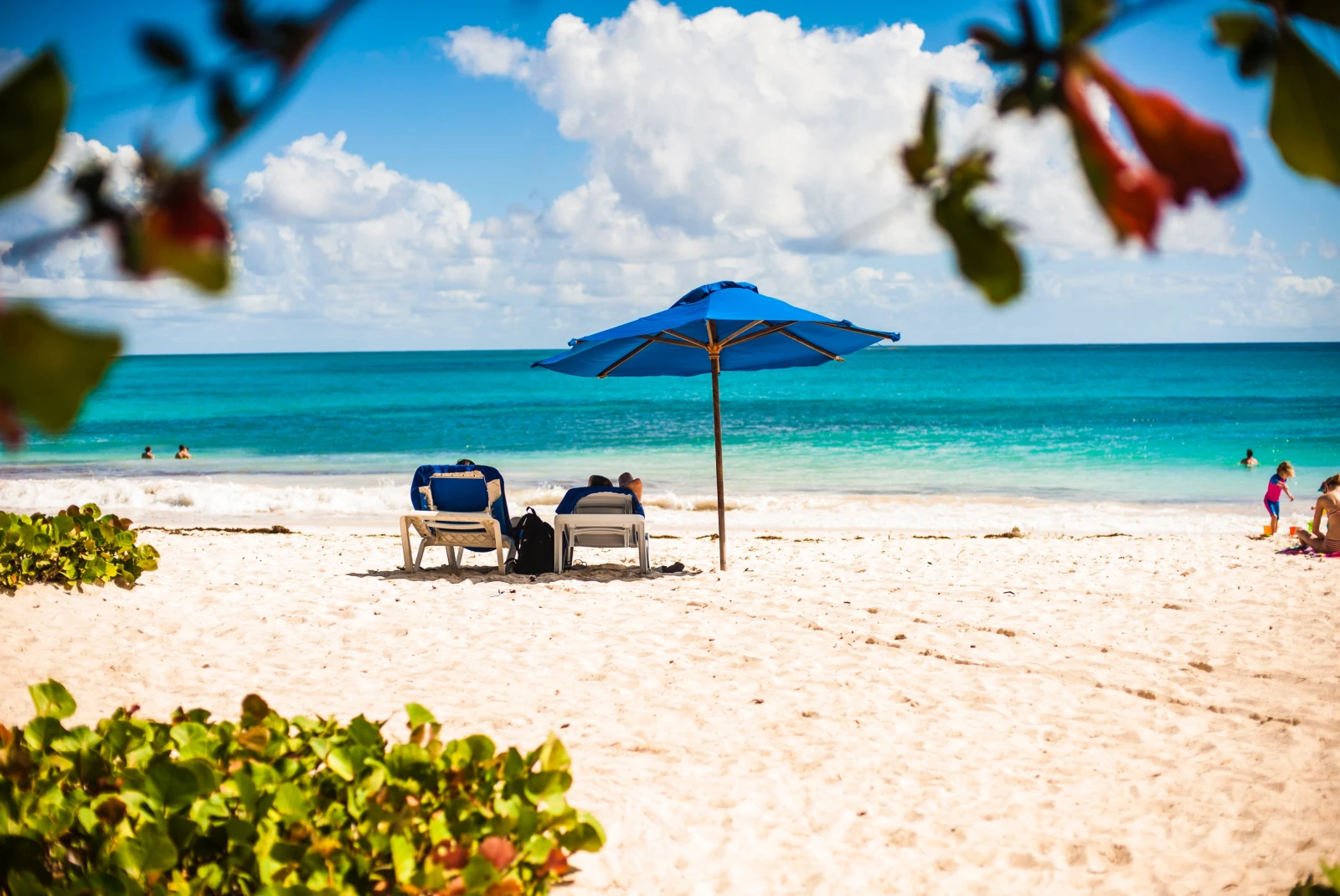 two beach chairs and an umbrella on white sand during daytime