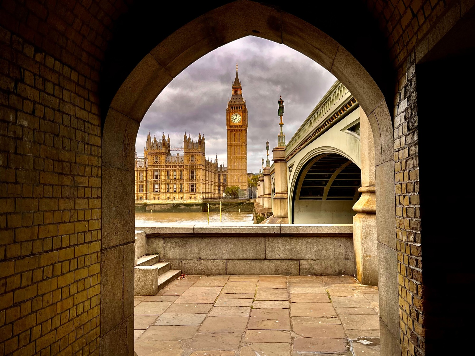 Clock tower and brown building from inside a cave like pathway.