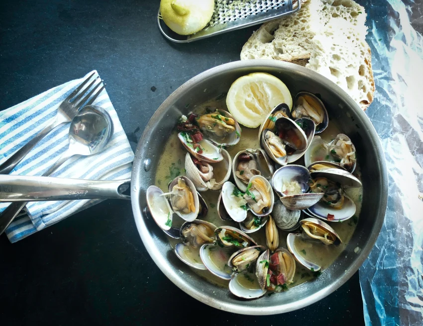 Pan of mussels with lemon and a side of bread next to a blue and white striped napkin and silverware