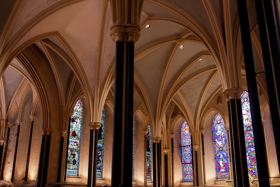 Inside a church with tan ceilings and tall black pillars with red blue and white stained glass
