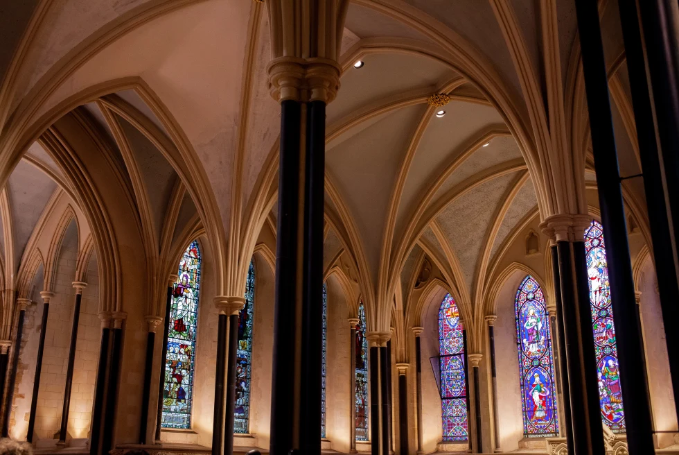Inside a church with tan ceilings and tall black pillars with red blue and white stained glass